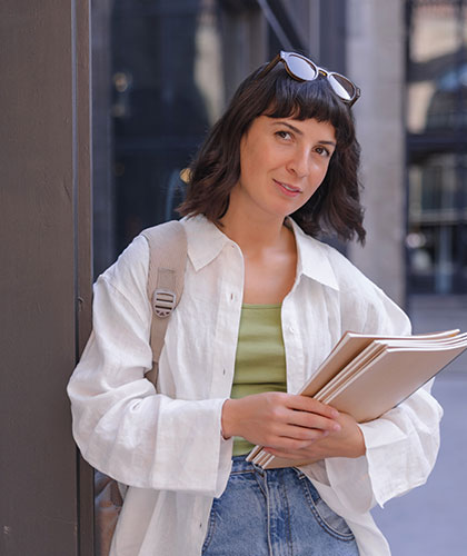 Mujer con camisa blanca, mochila y gafas de sol en la cabeza, sosteniendo unos documentos en una calle